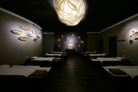 Elegant foot massagereception area at Happy Head Massage in Chula Vista, featuring modern lighting with shadow-casting fixtures, a sleek front desk, and comfortable leather seating. The room is designed with artistic wall accents and warm ambient lighting, creating a serene and inviting atmosphere.