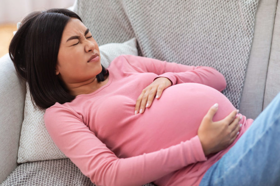 Pregnant woman in pain holding belly on couch