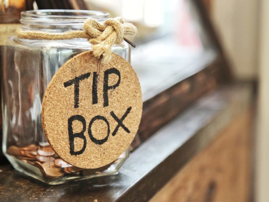 Glass jar with hemp rope tie tip box tag and few coins inside on wood counter