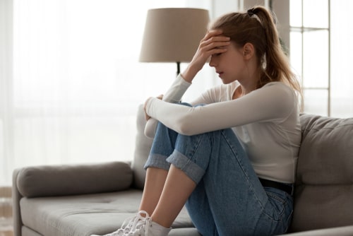 Young woman sitting on a couch curled up and holding her head