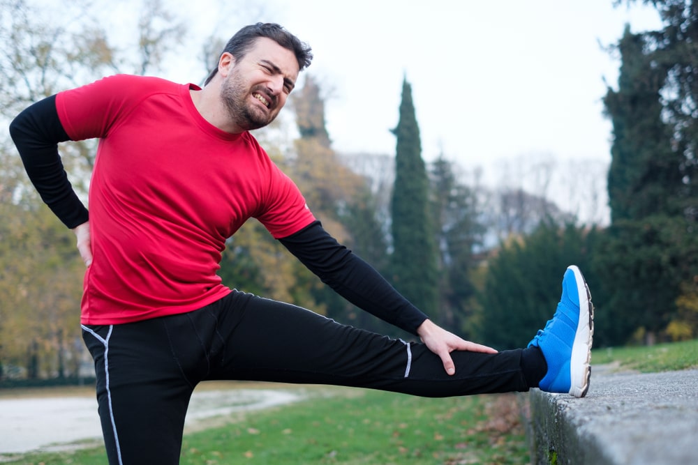 Man in red shirt grabbing his back in pain and stretching leg