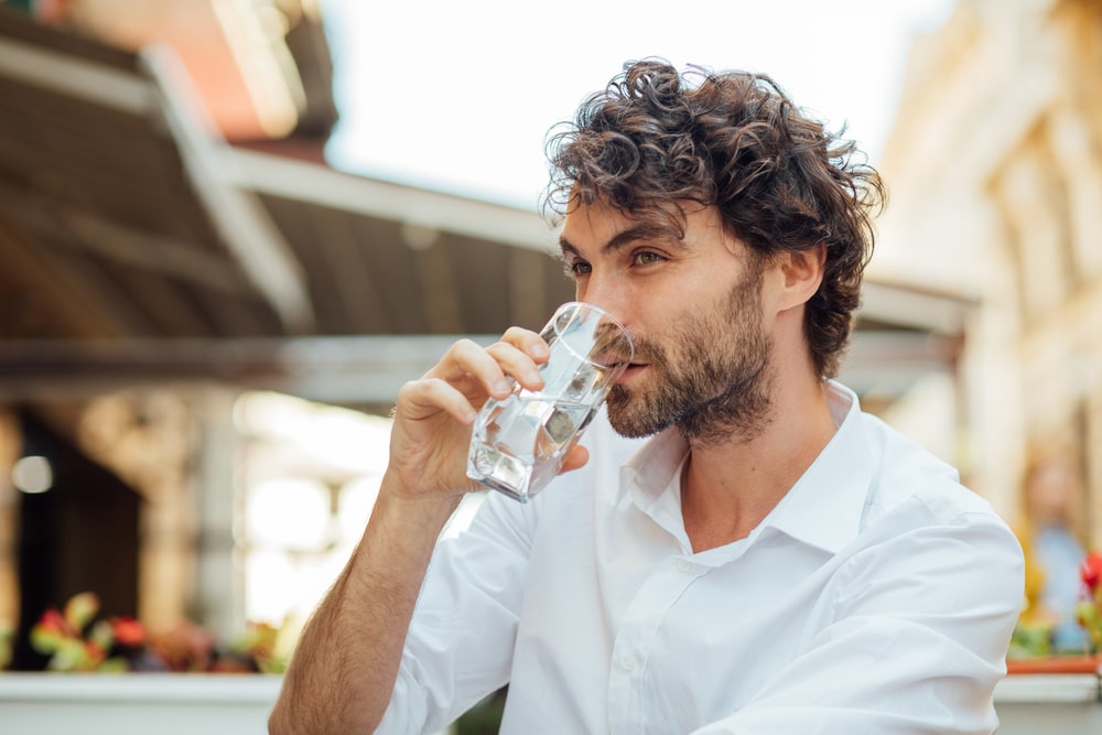 Man with curly hair drinking glass of water outdoors.