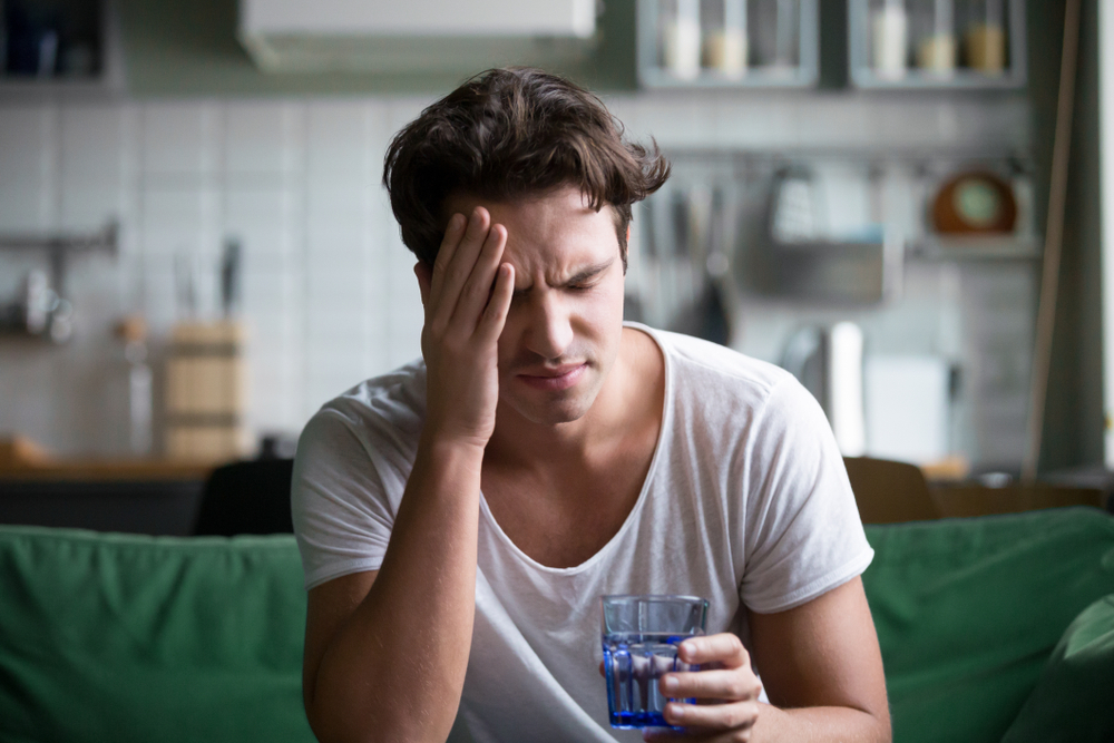 Man with headache sitting down with a glass of water in one hand
